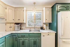 Una cocina con armarios blancos, encimera verde, pileta, lavavajillas y refrigerador.