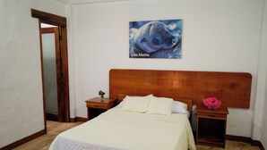 Ein Schlafzimmer mit einem Holzkopfende, einem Bett mit weißer Bettwäsche, einem Nachttisch mit einer Blumenvase und einem gerahmten Bild eines Robbenkopfes an der Wand.