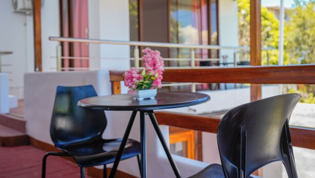 Ein Balkon mit Tisch und Stühlen, einem Blumentopf und einem Gebäude mit großen Fenstern und einem Balkongeländer.