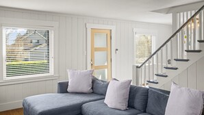 Ein modernes Wohnzimmer mit einem grauen Ecksofa, einer Holztür und einer Treppe mit Metallgeländer.