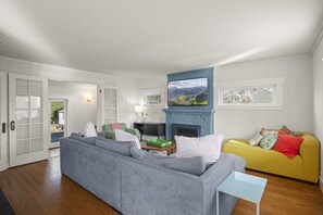 A living room with a grey sofa, a yellow sofa, a fireplace, and a television. - 3BR 2BA Flamingos West (Seattle)
