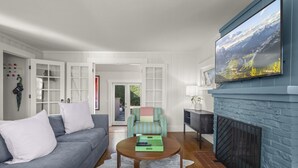 Ein Wohnzimmer mit grauem Sofa, einem gestreiften Sessel, einem Couchtisch, einem Kamin und einem großen Fenster mit Blick auf die Berge.