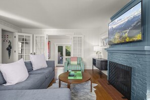A living room with a grey sofa, a striped armchair, a coffee table, a fireplace, and a large window with a mountain view. - 3BR 2BA Flamingos West (Seattle)