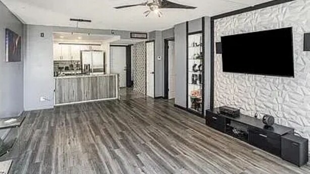 Un soggiorno moderno con una televisione a schermo piatto, una ventola a soffitto e una cucina sullo sfondo.
