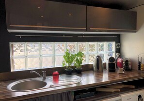 Eine moderne Küche mit Spüle aus Edelstahl, einem Fenster mit Milchglas und verschiedenen Küchengeräten auf der Arbeitsfläche.