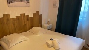 A neatly made bed with white linens, a wooden headboard, a nightstand with a lamp, and a window with curtains. - Flat « Étoile de Mer » Cannes center (Cannes)
