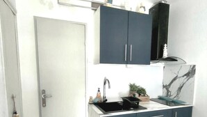 Una cocina compacta con una puerta blanca, gabinetes azul oscuro, un lavamanos negro y un salpicadero de mármol.