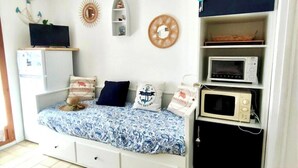 Un dormitorio con cama, televisor, microondas y repisas decorativas.