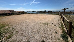 Un espacio con grava, una valla de madera, un farol y vistas a un lago y edificios al fondo.