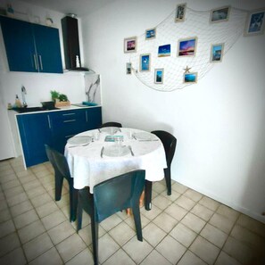 A dining area with a round table set for four, blue cabinets, and a wall decorated with framed photos. - House with terrace and pond access in Port-Leucate (Leucate)