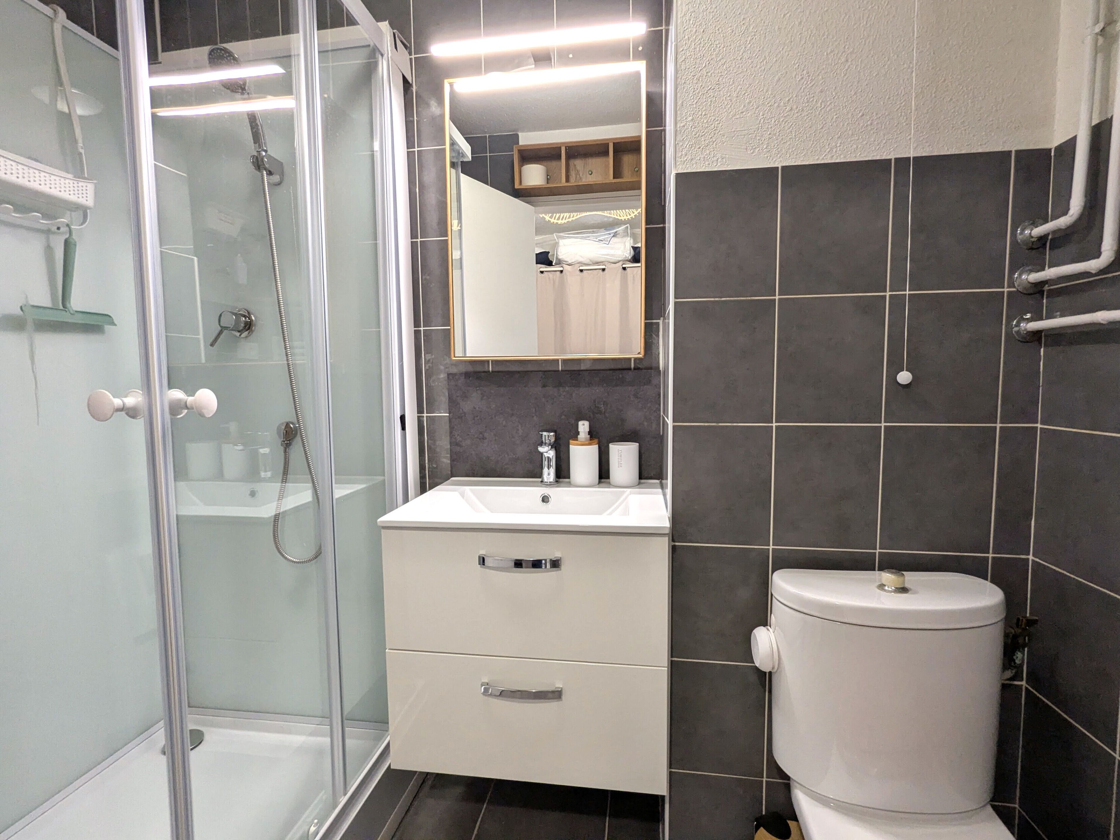 Un baño moderno con ducha de vidrio, un lavabo blanco y un inodoro.