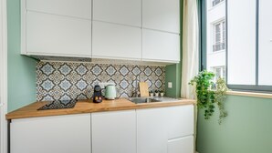 A kitchen with white cabinets, a patterned backsplash, a wooden countertop, a kettle, a coffee maker, and a potted plant.