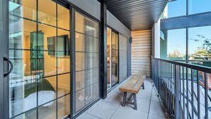 Un bâtiment moderne doté de grandes fenêtres en verre, d’un banc en bois et d’une rambarde en métal sur le balcon.