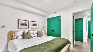 Une chambre à coucher avec un lit, une porte verte, des tableaux encadrés et un plafond blanc.