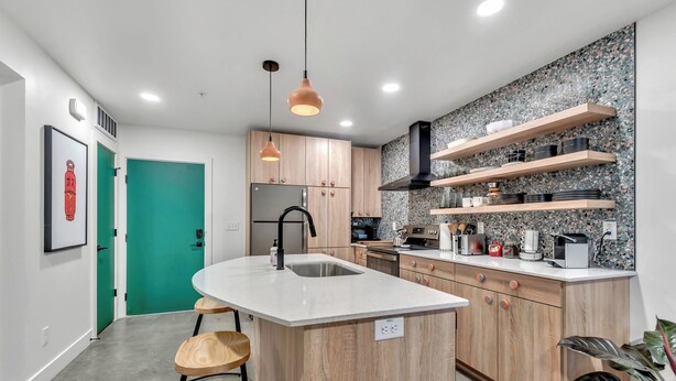 Une cuisine moderne avec un îlot central, des armoires en bois et une porte verte.