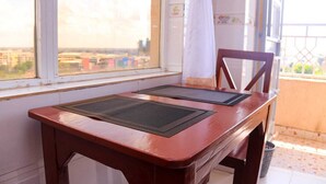 Een houten tafel met twee zwarte placemats, een stoel, een raam met uitzicht op gebouwen en een wit gordijn.