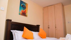 Een slaapkamer met een bed, oranje kussens, een houten garderobe en een schilderij aan de muur.