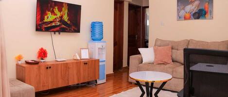 A living room with a sofa, a coffee table, a TV displaying a fireplace, a water dispenser, and a painting on the wall.