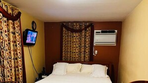 Ett hotellrum med en säng, en tv, en luftkonditionering och en mönstrad matta.