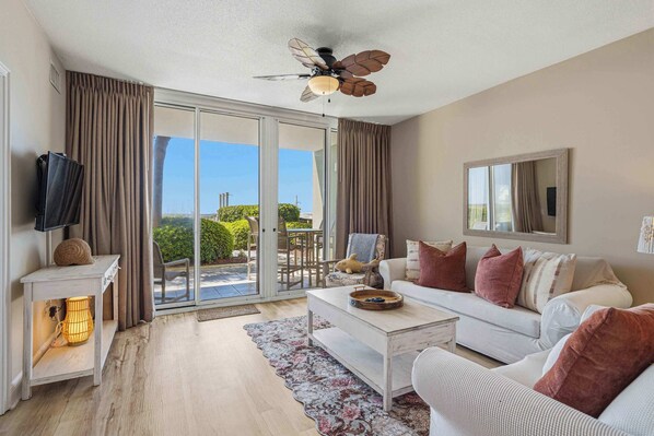 A modern living room with a sofa, coffee table, and a ceiling fan. - Gulf Front condo with Beach access and shared Pool (Fort Walton Beach)