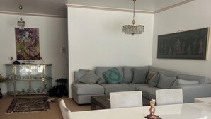 A living room with a grey sofa, a dining table with chairs, a chandelier, and a painting on the wall. - Top location in Brissago 2 room apartment with private beach access. Dogs allowed (Brissago)