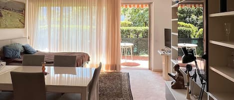 A modern living room with a dining area, a bookshelf, and a view of a garden.