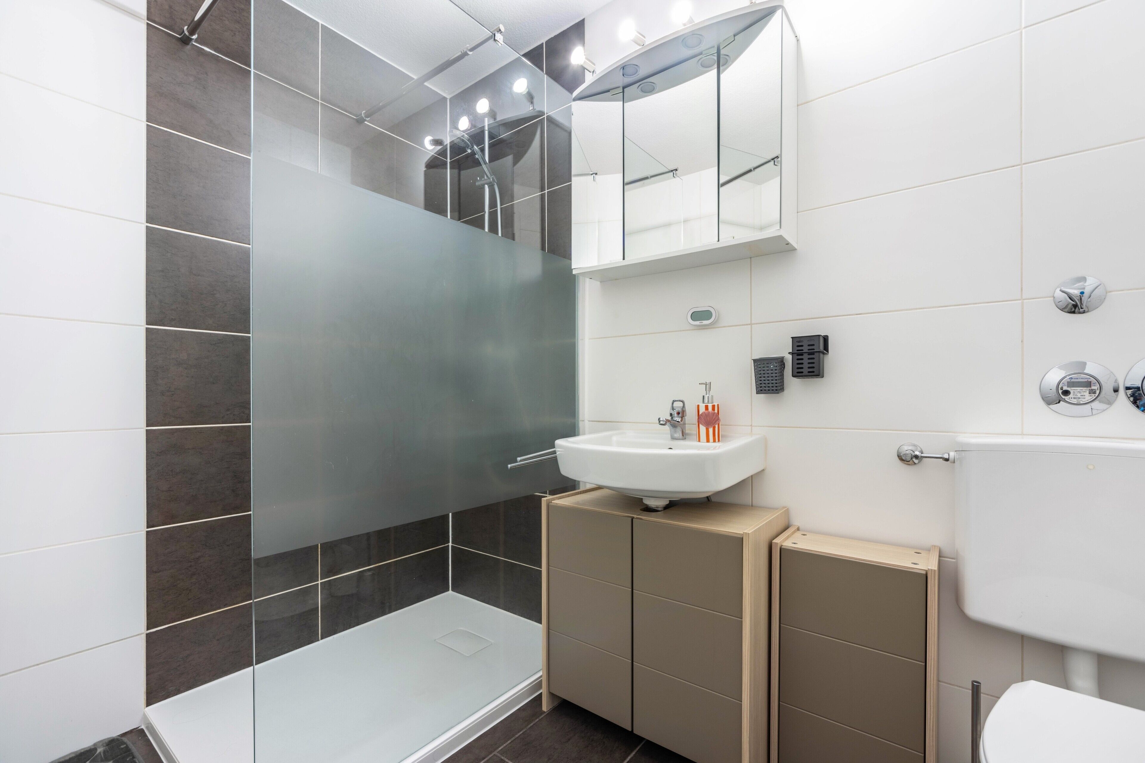 Un baño moderno con cabina de ducha de vidrio, un lavamanos blanco y un inodoro.