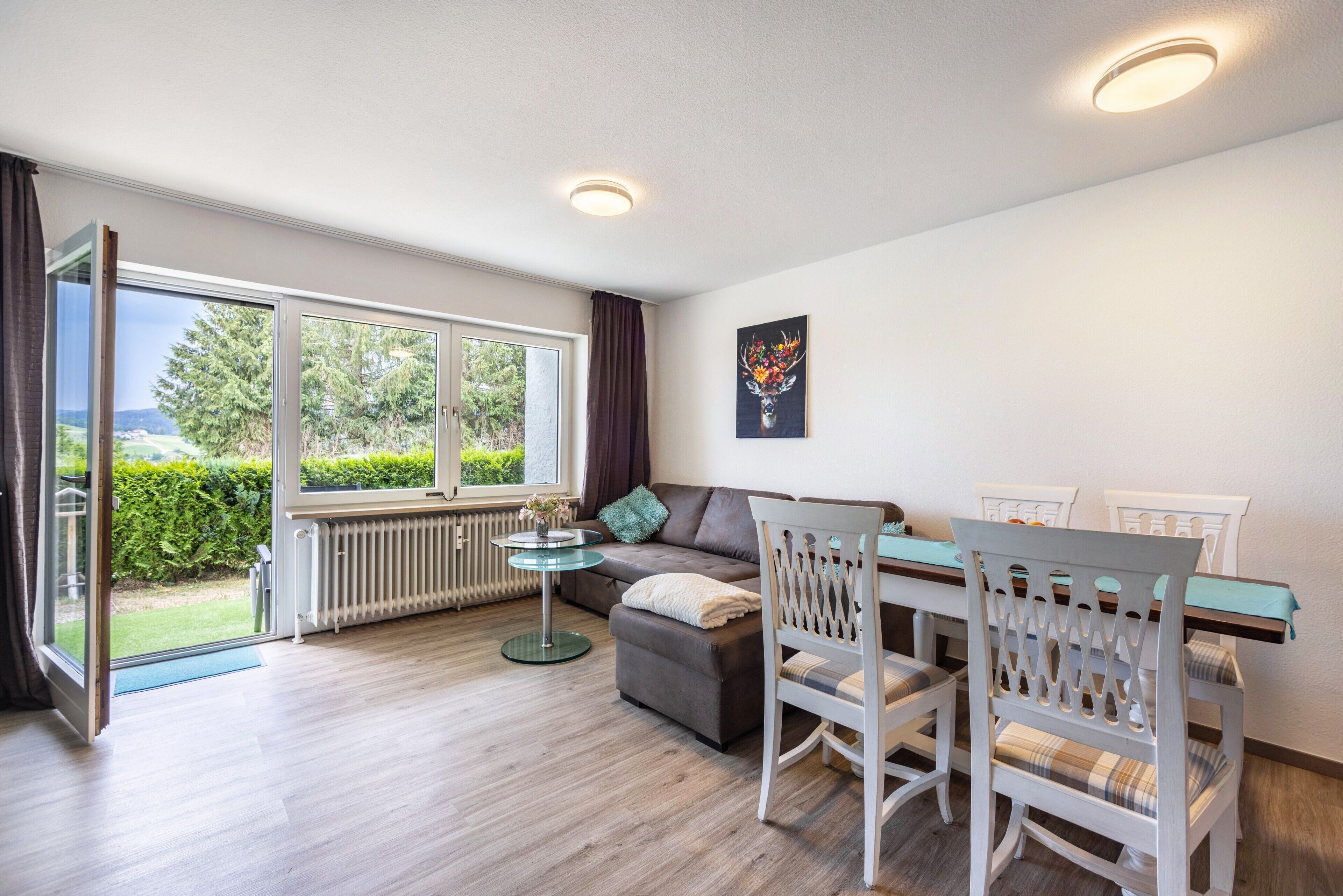 A room with a sofa, chairs, a table, a radiator, and a window with a view of greenery.