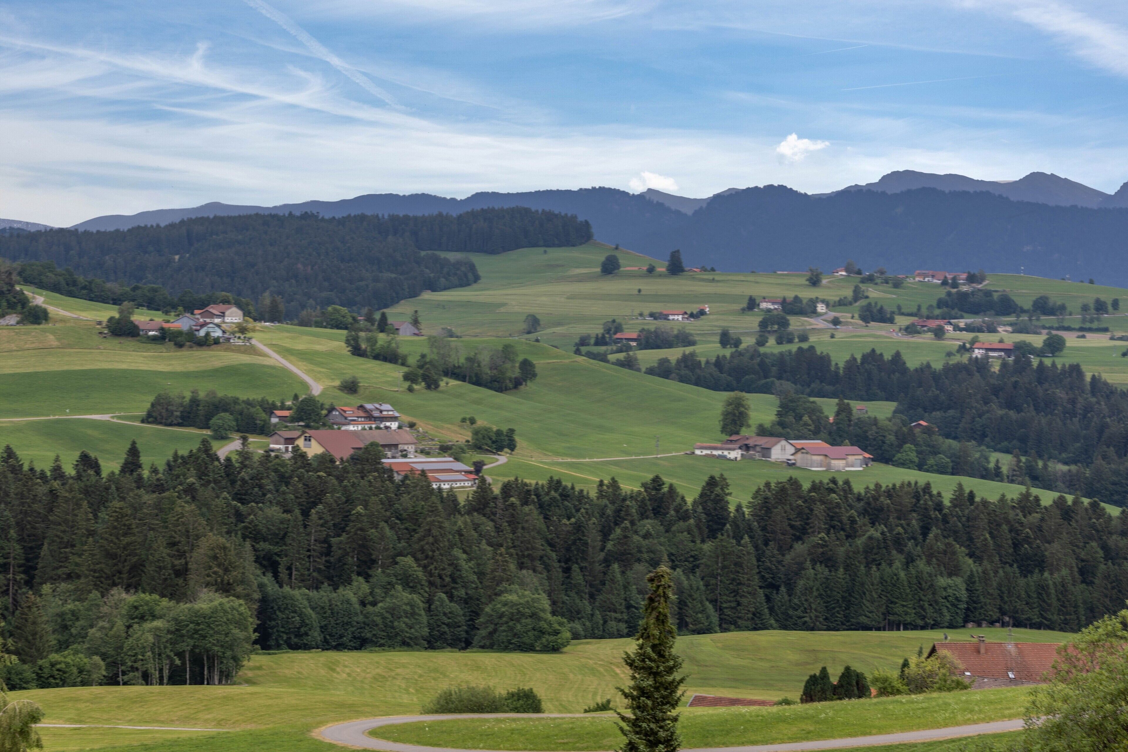 Un paysage rural caractérisé par des collines douces, des maisons dispersées et de vastes forêts.