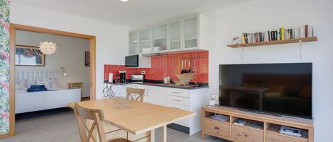 A modern kitchen with white cabinets, a red backsplash, and a built-in TV.