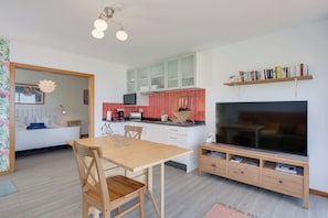Una cocina moderna con armarios blancos, salpicadero rojo y televisor integrado.