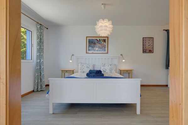 A bedroom with a white bed, two bedside tables, a hanging light fixture, a window with curtains, and a framed picture on the wall. - Sea Sky Studio by Holiday Rental Madeira (Ponta do Sol)