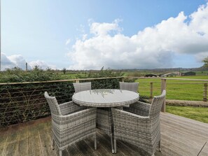 Ein runder Tisch mit Korbstühlen auf einer Holzterrasse, mit Blick auf eine ländliche Landschaft mit Feldern und Scheunen.