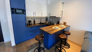 A modern kitchen with blue cabinets, a wooden island with stools, and a built-in microwave. - Stylish One Bedroom Retreat Budva (Budva)