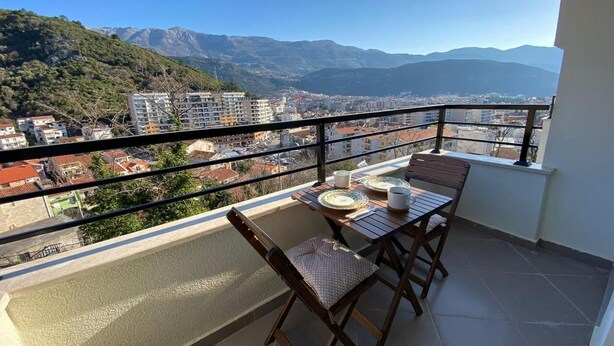 A balcony with a table and chairs, overlooking a cityscape and mountains. - Stylish One Bedroom Retreat Budva (Budva)