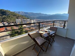 A balcony with a table and chairs, overlooking a cityscape and mountains. - Stylish One Bedroom Retreat Budva (Budva)