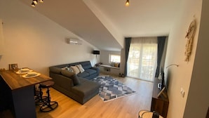 A modern living space with a sofa, a dining area with stools, a patterned rug, and a staircase leading to an upper level. - Stylish One Bedroom Retreat Budva (Budva)