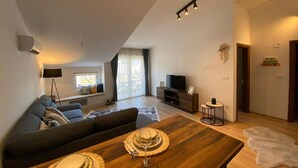 A modern living room with a sofa, dining table, and a TV. - Stylish One Bedroom Retreat Budva (Budva)
