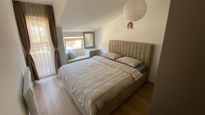 A bedroom with a bed, a window with curtains, a bedside table, and a wall-mounted light fixture. - Stylish One Bedroom Retreat Budva (Budva)