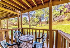 Ein überdachter Außenbereich mit Holzterrasse, zwei Plastikstühlen und einem Tisch mit Mosaikmuster.