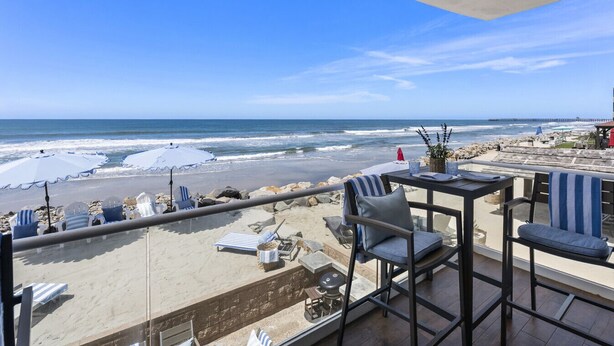 Un balcón con vista a la playa, mobiliario exterior y una mesa.