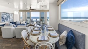 Un comedor moderno con vistas al océano, que presenta una mesa redonda con individuales tejidos, sillas de mimbre y un ventilador de techo.