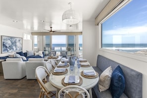 A modern dining area with a view of the ocean, featuring a round table with woven placemats, wicker chairs, and a ceiling fan. - New Beachfront Home | Walk to Pier, Dining & Coffee | Oceanside CA (Oceanside)