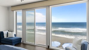 Una habitación con un gran ventanal corredizo que da a una vista de la playa, un sofá azul y una cama con colcha azul.