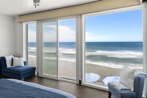 A room with a large sliding glass door leading to a beach view, a blue sofa, and a bed with a blue quilt. - New Beachfront Home | Walk to Pier, Dining & Coffee | Oceanside CA (Oceanside)