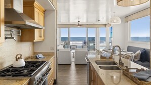Una cocina con estufa, lavamanos y grandes ventanales con vistas al océano.