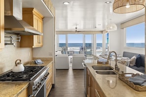 A kitchen with a stove, sink, and large windows overlooking the ocean. - New Beachfront Home | Walk to Pier, Dining & Coffee | Oceanside CA (Oceanside)