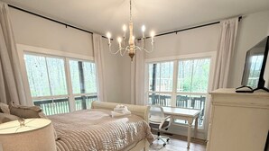 Een slaapkamer met een bed, nachtkastje, lamp en uitzicht op een terras door grote ramen.