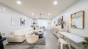 Una sala de estar moderna con un sofá, sillones, una mesa de centro y un comedor con una mesa y sillas blancas.