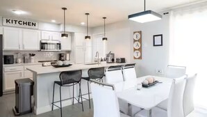 Una cocina moderna con armarios blancos, una isla central, taburetes negros y luminarias colgantes.